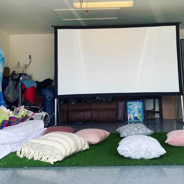 A garage with a projector screen and pillows on the floor, perfect for a Texas-themed party rental.