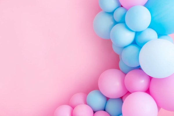 Pink and blue balloons create a festive atmosphere against a pink backdrop.