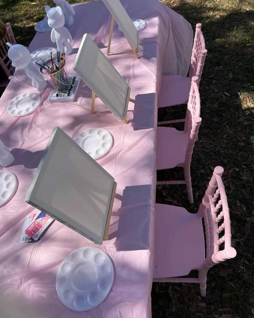 A table set up for a painting party with pink chairs, available through a Texas party rental.