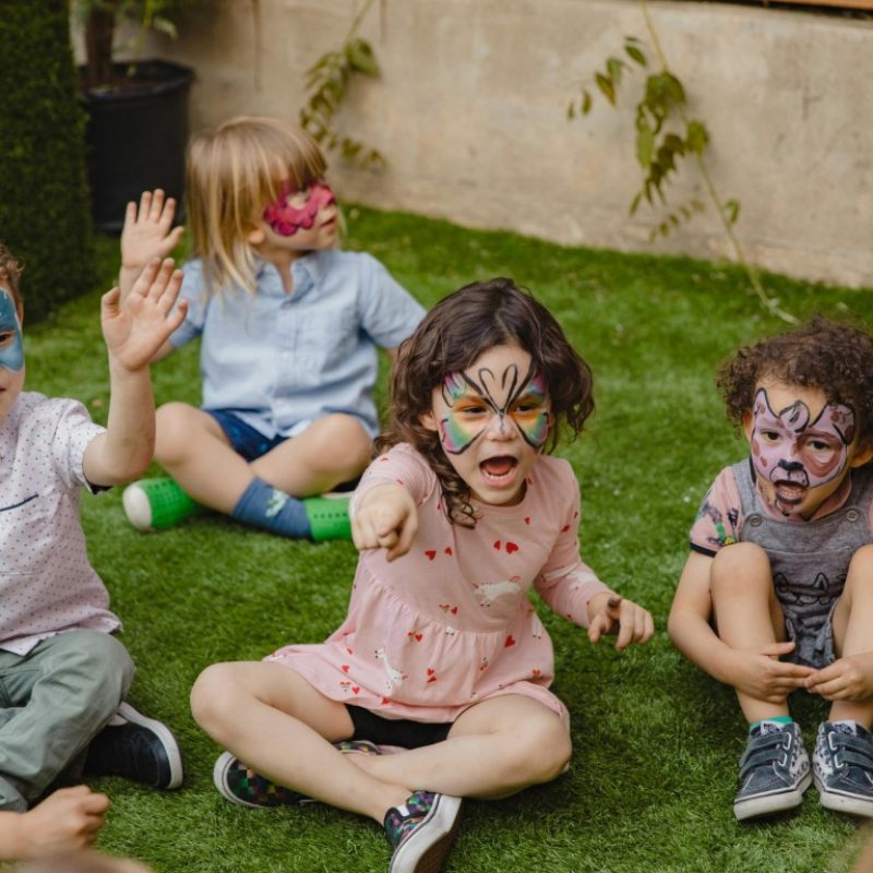 A group of children sitting on the grass with paint on their faces at a Texas party rental.
